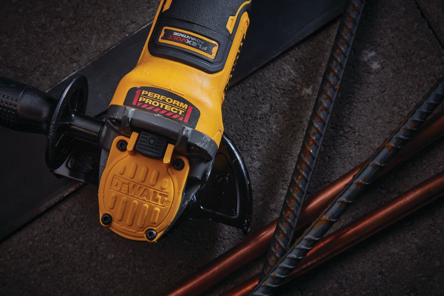 Primer plano de una amoladora angular inalámbrica DEWALT colocada sobre una superficie rugosa junto a unas varillas de metal. La herramienta es amarilla y negra, con las etiquetas 'PERFORM PROTECT' y 'DEWALT' claramente visibles.