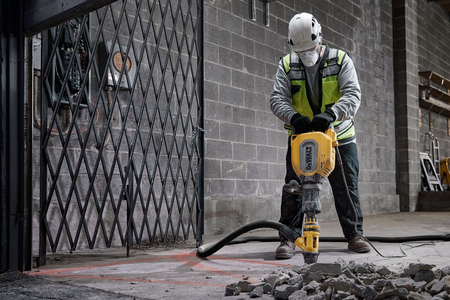 Un trabajador de la construcción con equipo de seguridad opera un martillo demoledor DEWALT D25911K, rompiendo concreto en un sitio industrial.