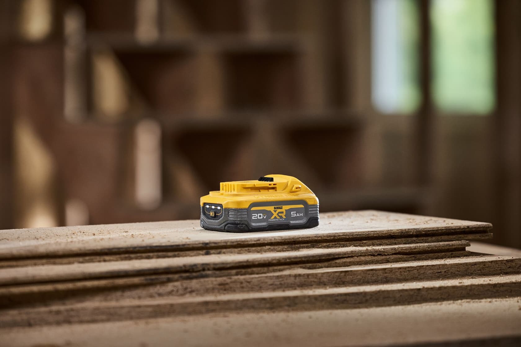 A DEWALT 20V XR lithium-ion battery with a 5Ah capacity, placed on a stack of wooden boards in a workshop setting.