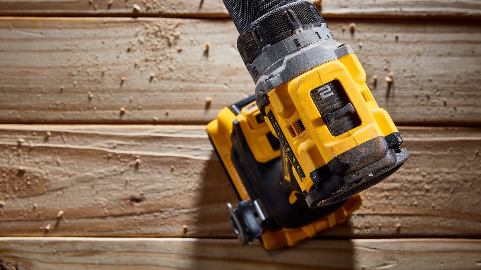 Vista de primer plano de un taladro inalámbrico DEWALT utilizado sobre una superficie de madera con virutas de madera alrededor.