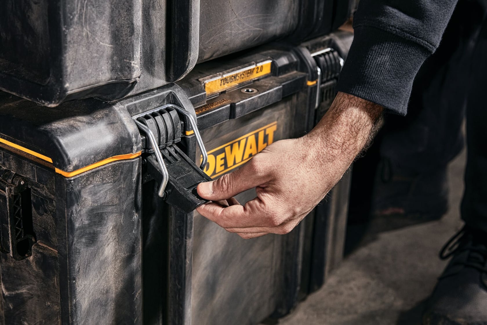Primer plano de la mano de una persona abriendo el cierre de una caja de almacenamiento de herramientas negra DEWALT TOUGHSYSTEM 2.0.
