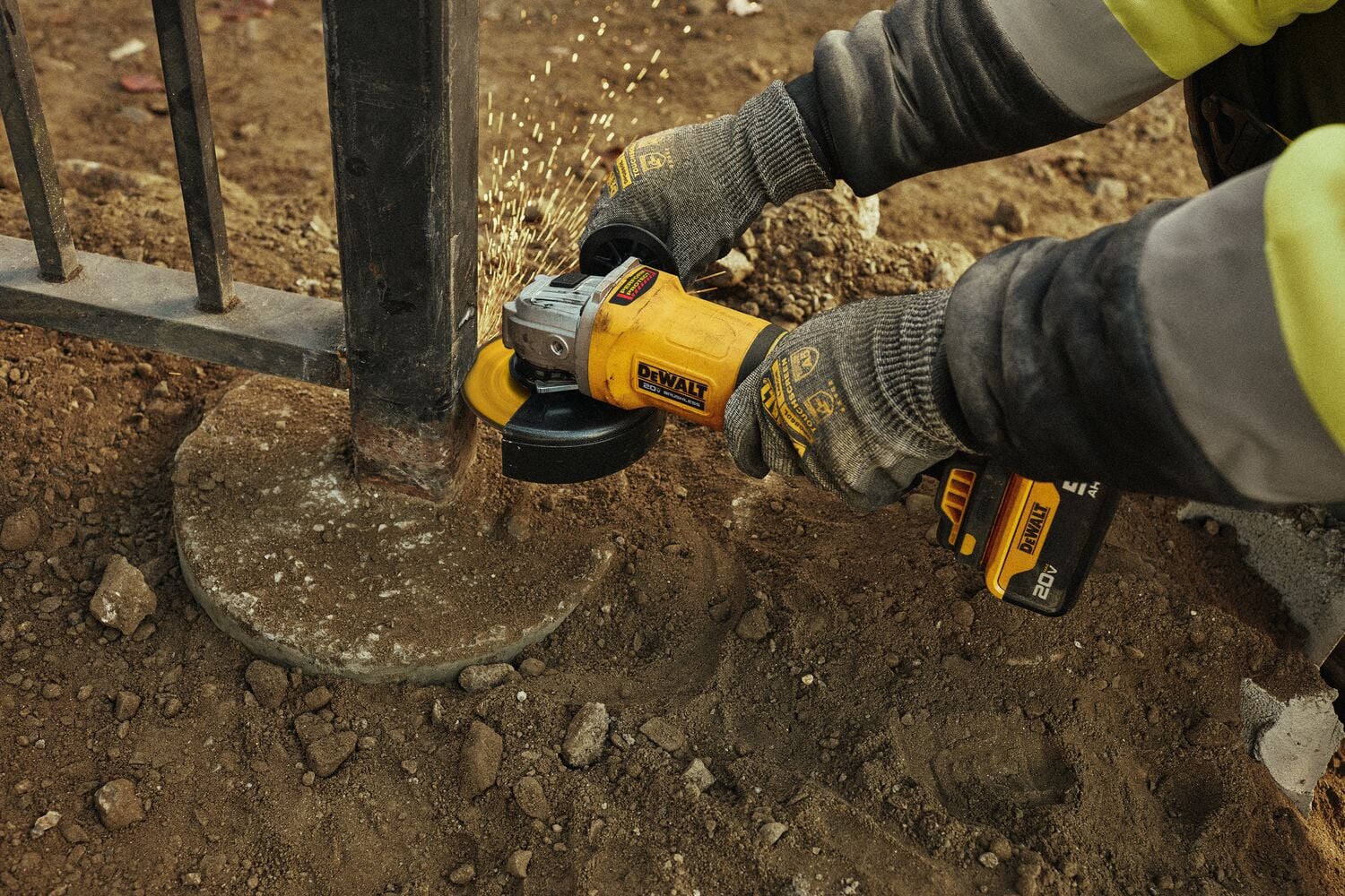 Persona con guantes usando una amoladora angular inalámbrica amarilla DEWALT para lijar metal en un poste de cerca exterior, con chispas volando.