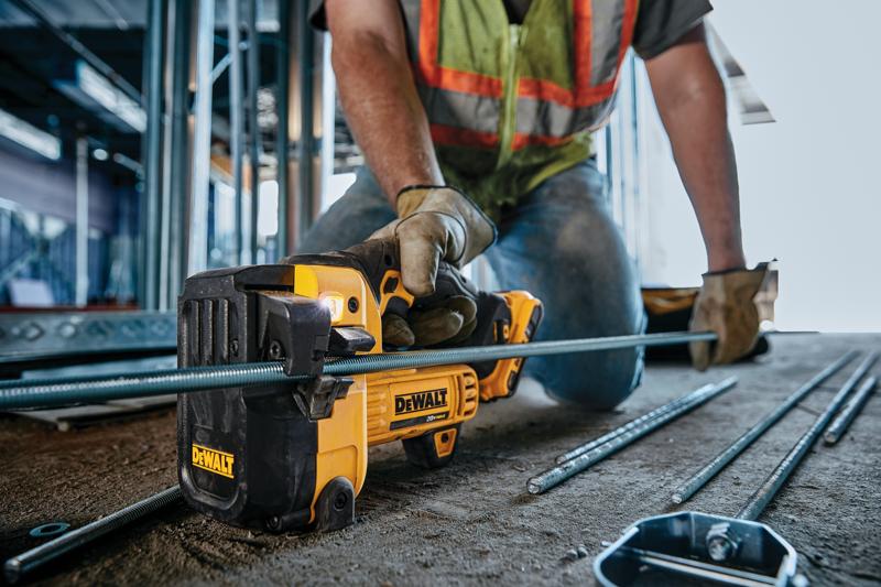 Una persona con guantes de trabajo y chaleco de seguridad utiliza un cortador de varilla roscada DEWALT DCS350B para cortar una varilla metálica en una obra. La herramienta es amarilla y negra, y varias varillas metálicas están en el suelo.