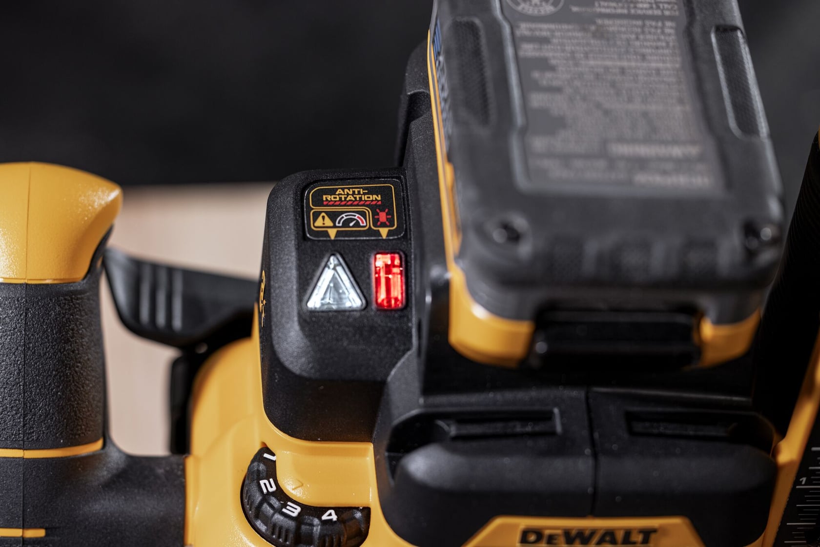 Close-up of a DEWALT handheld power tool, showing the control panel with indicator lights, labeled warning stickers with anti-rotation text and icons, and a visible part of an attached battery pack.