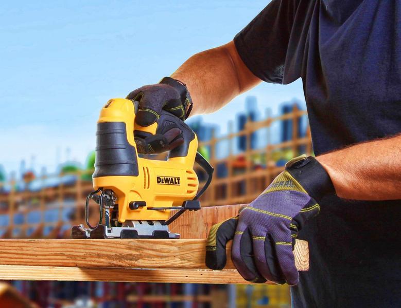 Una persona con guantes de protección utiliza una sierra caladora amarilla DEWALT para cortar un trozo de madera al aire libre.