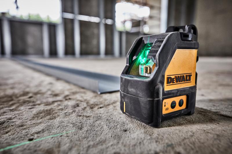 Un nivel láser verde DEWALT DW088CG colocado sobre un piso de concreto en un sitio de construcción, proyectando una línea láser verde para alineación.