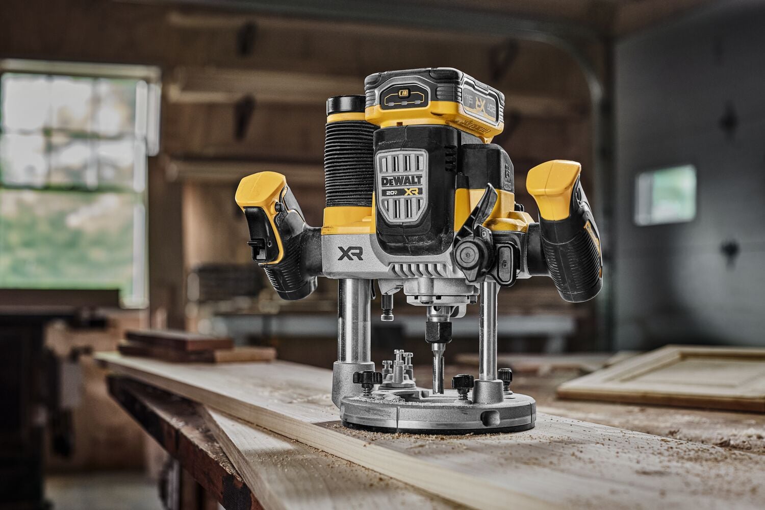 A DEWALT cordless plunge router, model DCW620B, shown in a workshop setting on a wooden surface with wood shavings around it. The router features a yellow and black design typical of DEWALT products.