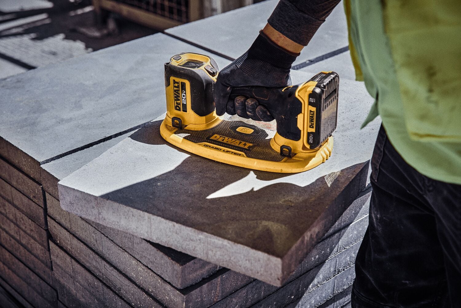 Una persona usando un vibrador de concreto inalámbrico amarillo y negro DEWALT sobre una pila de losas de concreto en un sitio de construcción.