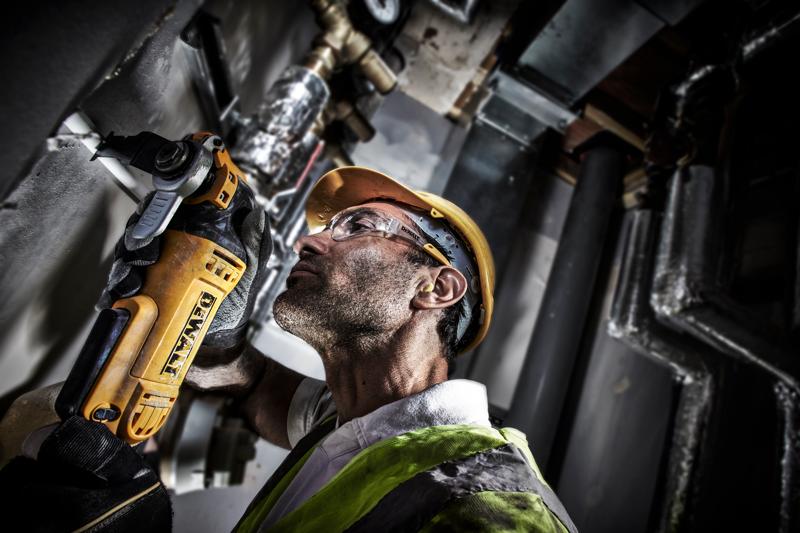 Un trabajador con equipo de seguridad utiliza una herramienta eléctrica DEWALT DWE315 para cortar una pared en un entorno industrial. El rostro del trabajador está difuminado para preservar la privacidad.