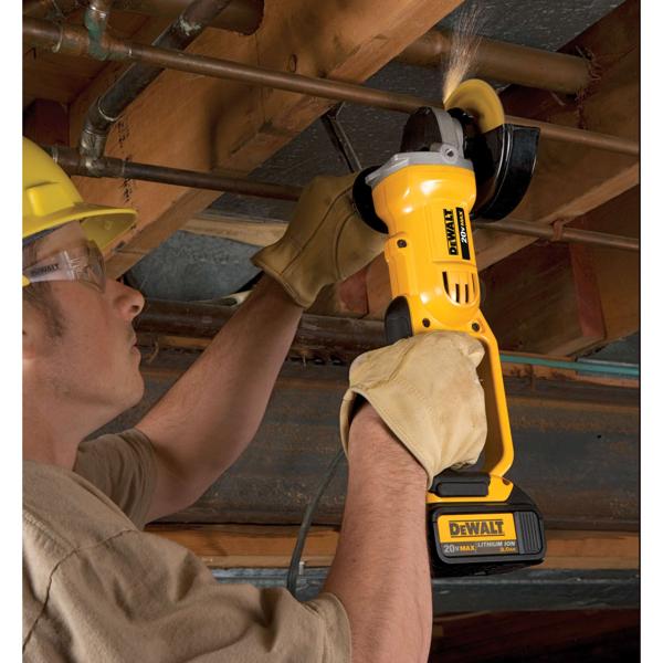 Una persona con guantes protectores utiliza una amoladora angular inalámbrica DEWALT amarilla para cortar una tubería de metal bajo un techo de madera. La amoladora funciona con batería y produce chispas al cortar.