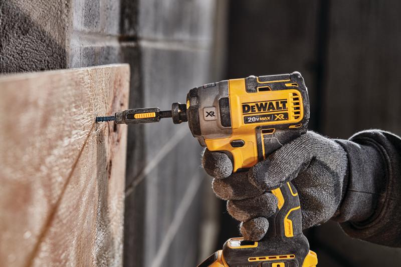 Una persona con guantes de trabajo utiliza un destornillador de impacto inalámbrico DEWALT 20V MAX XR amarillo y negro para atornillar un tornillo en una tabla de madera.