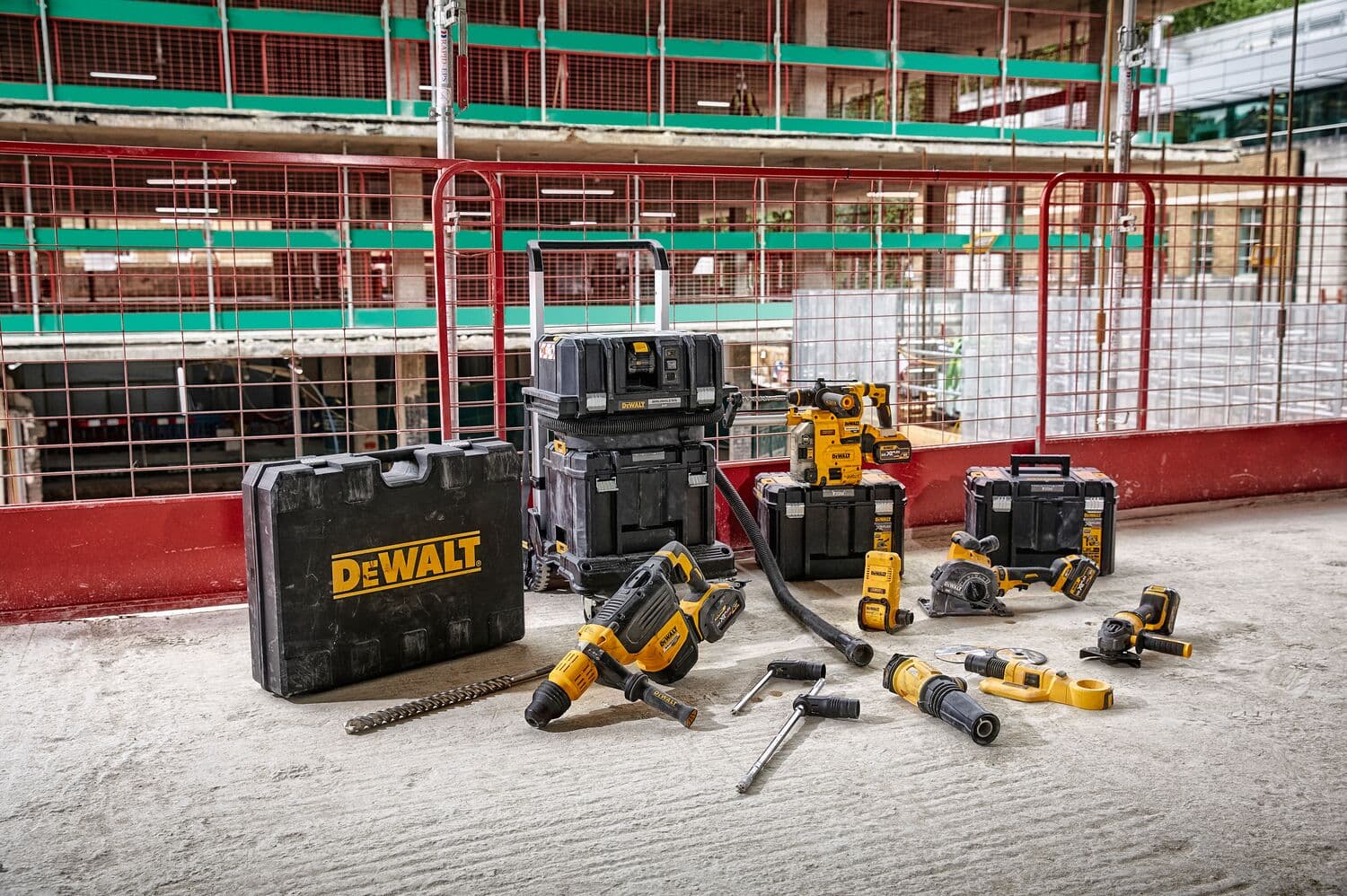 Una colección de herramientas eléctricas y cajas de herramientas DEWALT está exhibida sobre el suelo de una obra de construcción. Incluye taladros, una amoladora y otras máquinas portátiles. La escena muestra varios estuches y cajas de almacenamiento DEWALT en color negro y amarillo, con un edificio en construcción al fondo.