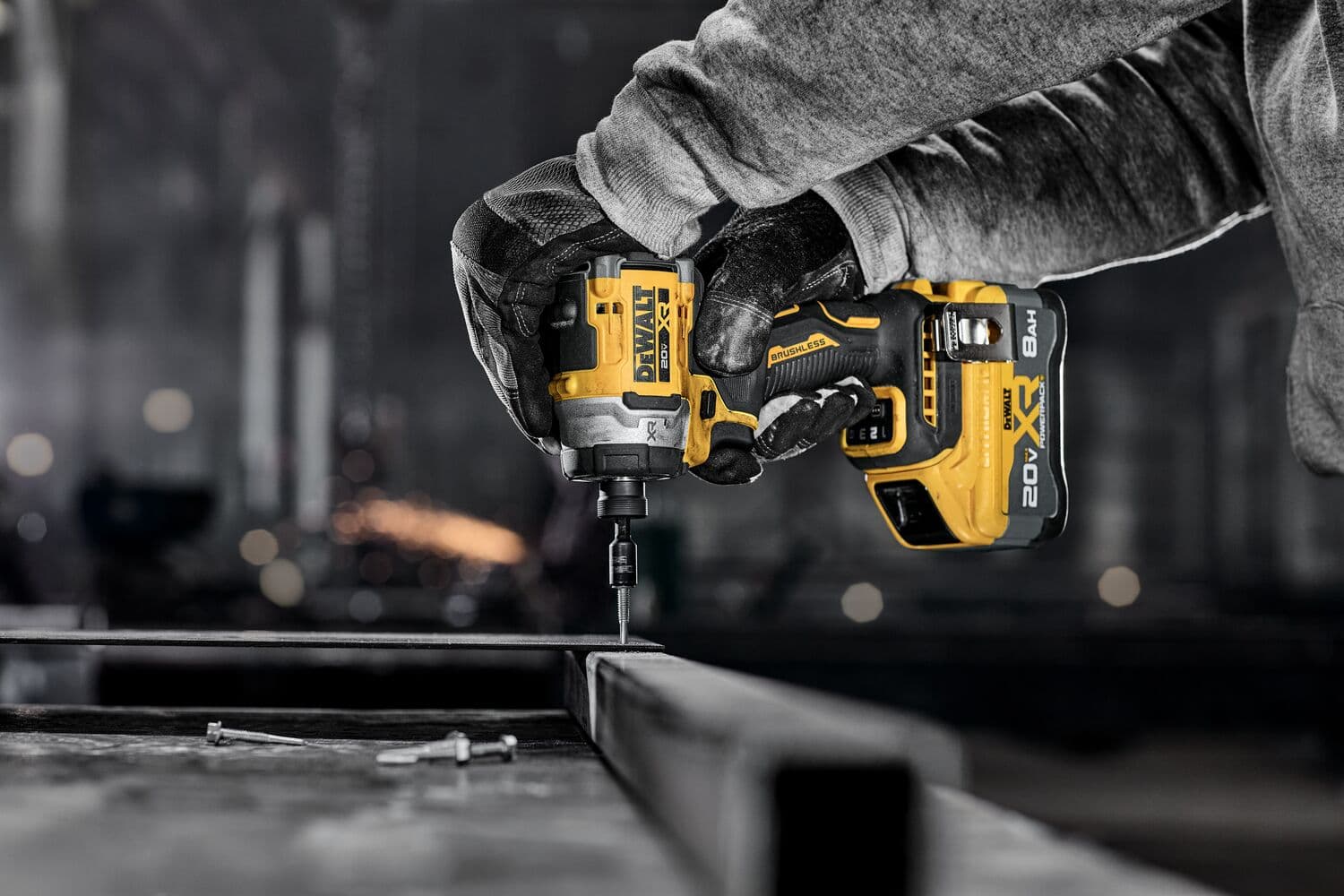 A person wearing gloves uses a DEWALT 20V cordless impact driver to fasten a screw into a metal frame in an industrial setting.
