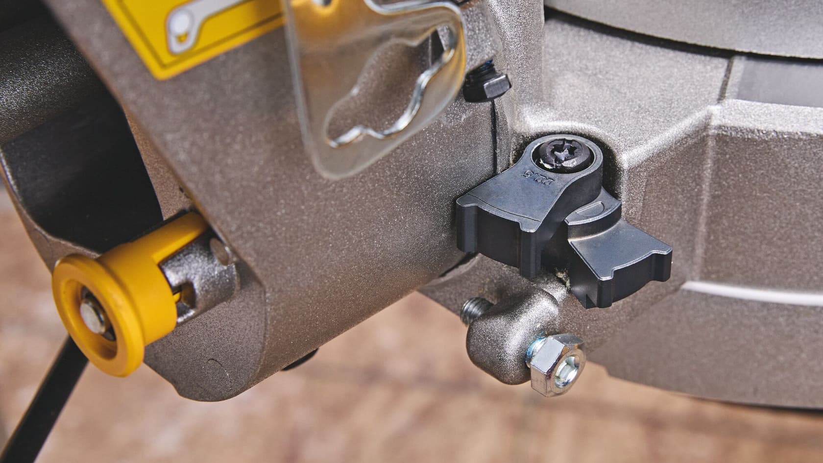 Vista de cerca de una parte de una herramienta eléctrica DEWALT, mostrando perillas de ajuste, una rueda amarilla y un perno de metal.