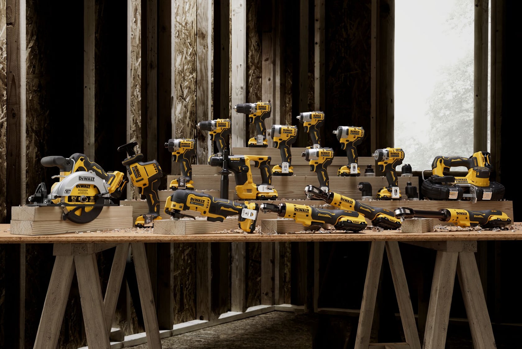 Una variedad de herramientas eléctricas DEWALT, incluyendo taladros, sierras y destornilladores, exhibidas sobre mesas de madera dentro de un taller con paredes de madera sin terminar.
