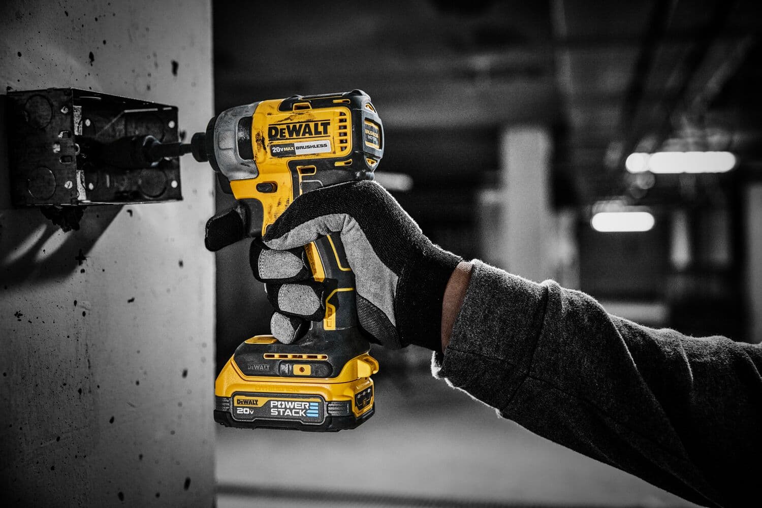 Una persona con guantes usa un taladro inalámbrico amarillo y negro DEWALT de 20V para atornillar en una caja eléctrica montada en la pared.
