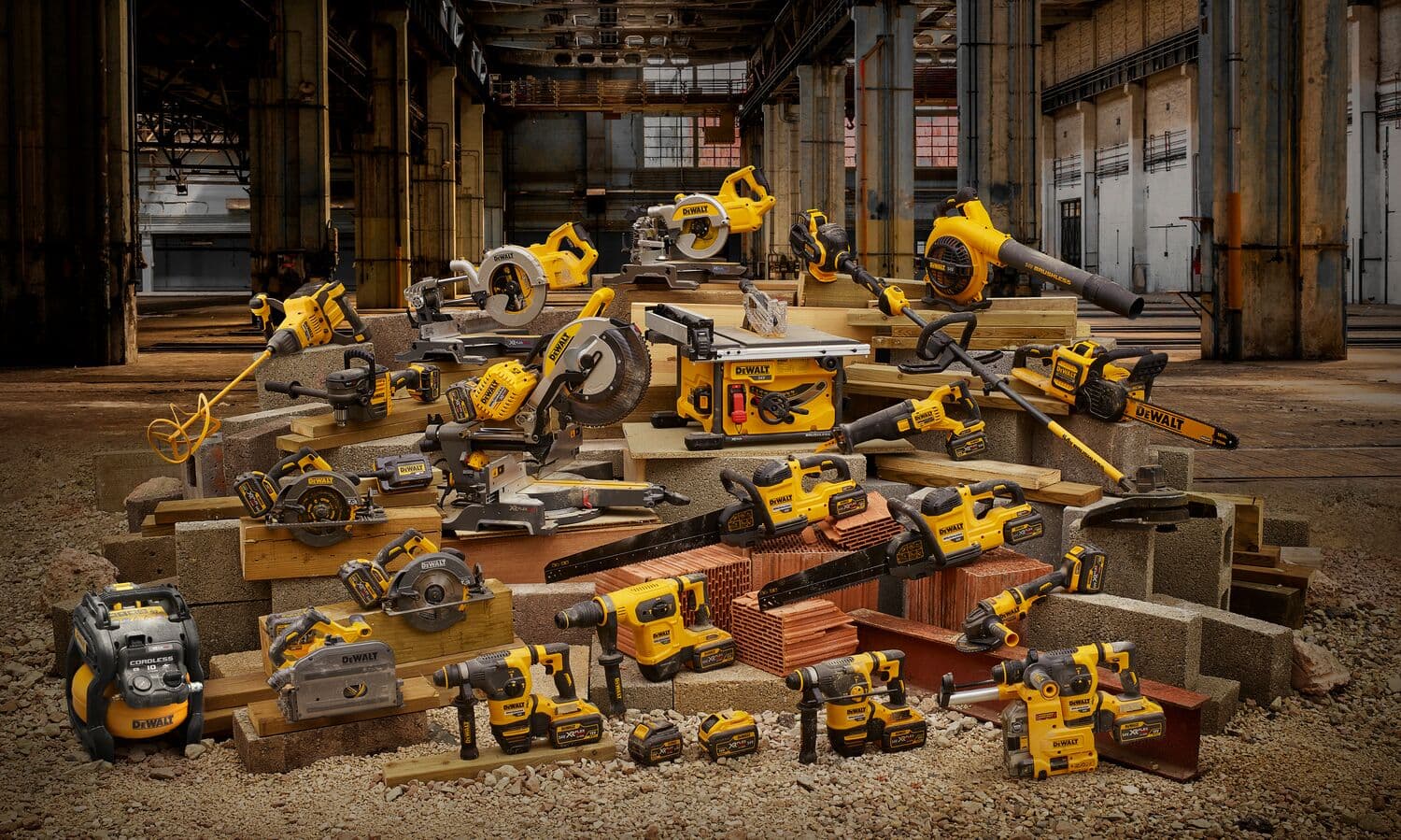 Un grupo de varias herramientas eléctricas DEWALT, incluyendo taladros, sierras, amoladoras y sopladores, dispuestas sobre materiales de construcción dentro de un edificio industrial.