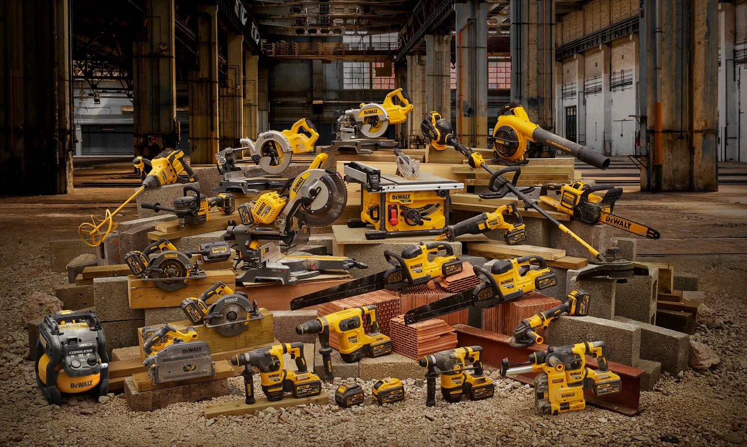 Un grupo de varias herramientas eléctricas DEWALT, incluyendo taladros, sierras, amoladoras y sopladores, dispuestas sobre materiales de construcción dentro de un edificio industrial.