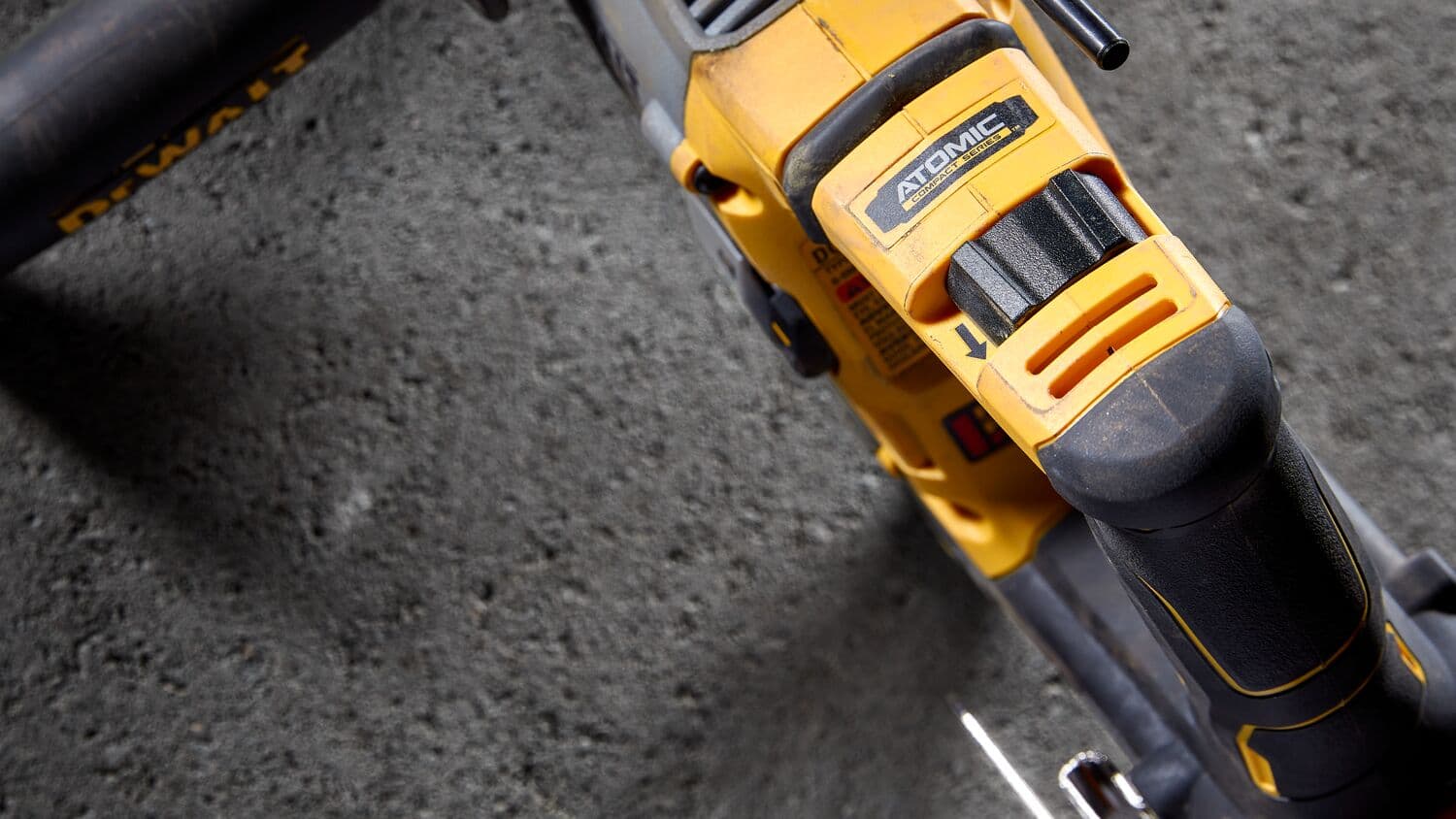 Vista en primer plano de una herramienta eléctrica DEWALT de la serie Atomic sobre una superficie de concreto, mostrando detalles del mango y el etiquetado.