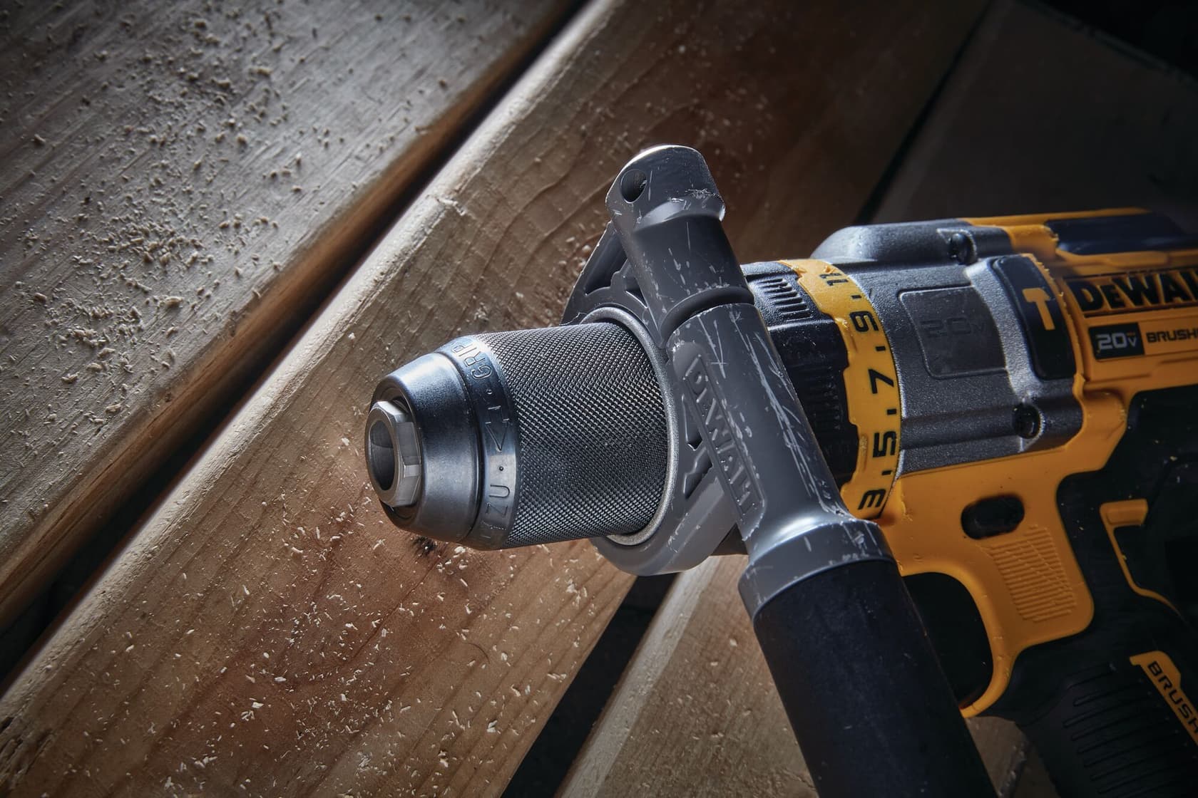 Vista de primer plano de un taladro inalámbrico DEWALT DCD999B con empuñadura texturizada y mango lateral ajustable, apoyado sobre tablas de madera.