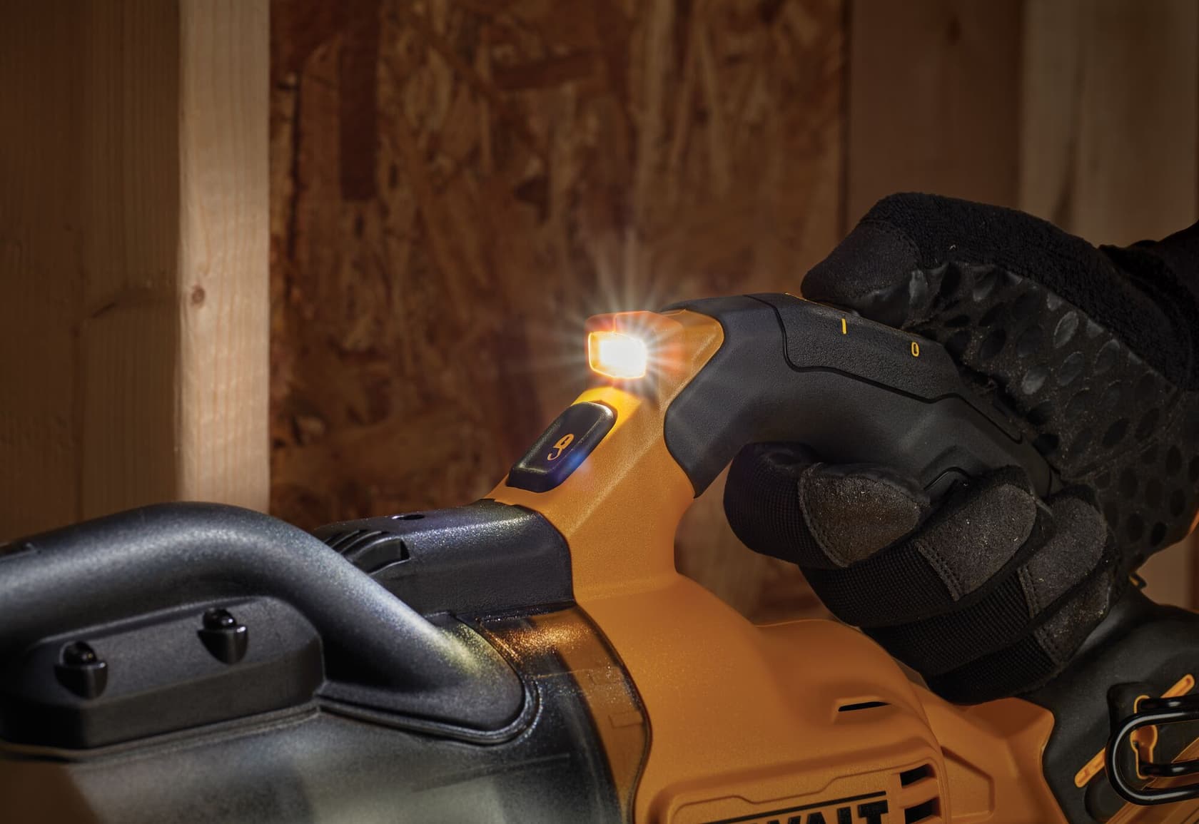 Primer plano de una mano enguantada operando una herramienta eléctrica DEWALT amarilla y negra con una luz LED integrada encendida, en un taller.