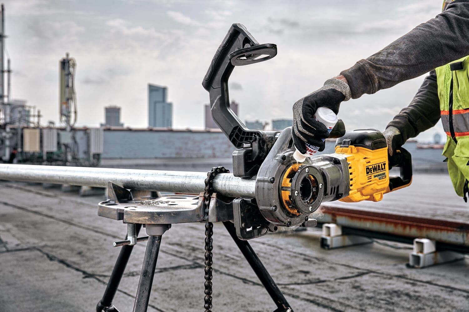 Un trabajador utiliza una roscadora eléctrica DEWALT para roscar una tubería de metal fijada en un soporte trípode en un sitio industrial al aire libre.