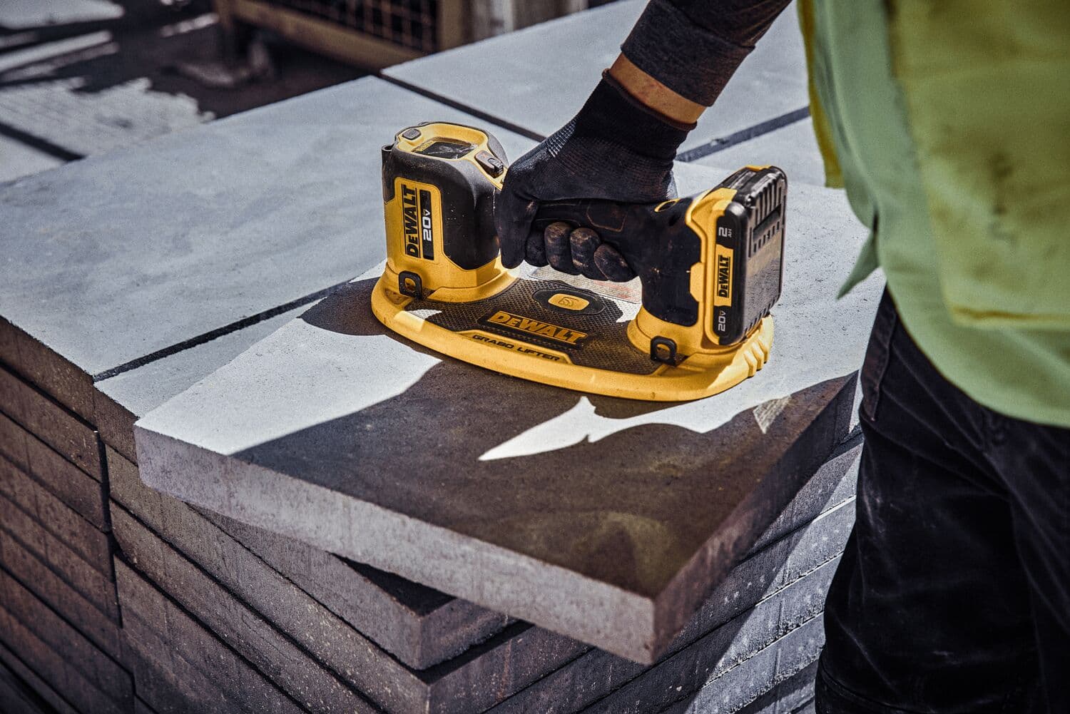 Una persona usando un vibrador de concreto inalámbrico amarillo y negro DEWALT sobre una pila de losas de concreto en un sitio de construcción.