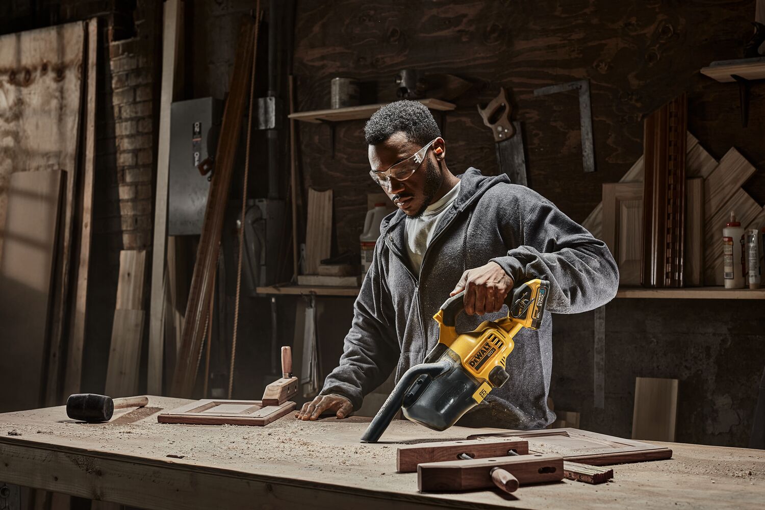 Male using DEWALT 20 MAX* Hand Vacuum vacuuming up wood dust, saw dust, wood chips. DEWALT Power Stack battery is being used.